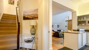 A staircase with a patterned floor, a lamp, a painting, and a kitchen area with cabinets and a toaster. - 4 Bed in Keswick (oc-89258) (Keswick)