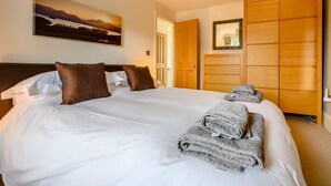 A hotel room with a large bed, a painting on the wall, and a wooden wardrobe. - 4 Bed in Keswick (oc-89258) (Keswick)