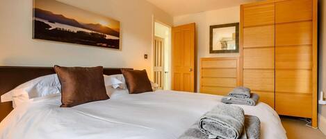 A hotel room with a large bed, a painting on the wall, and a wooden wardrobe.