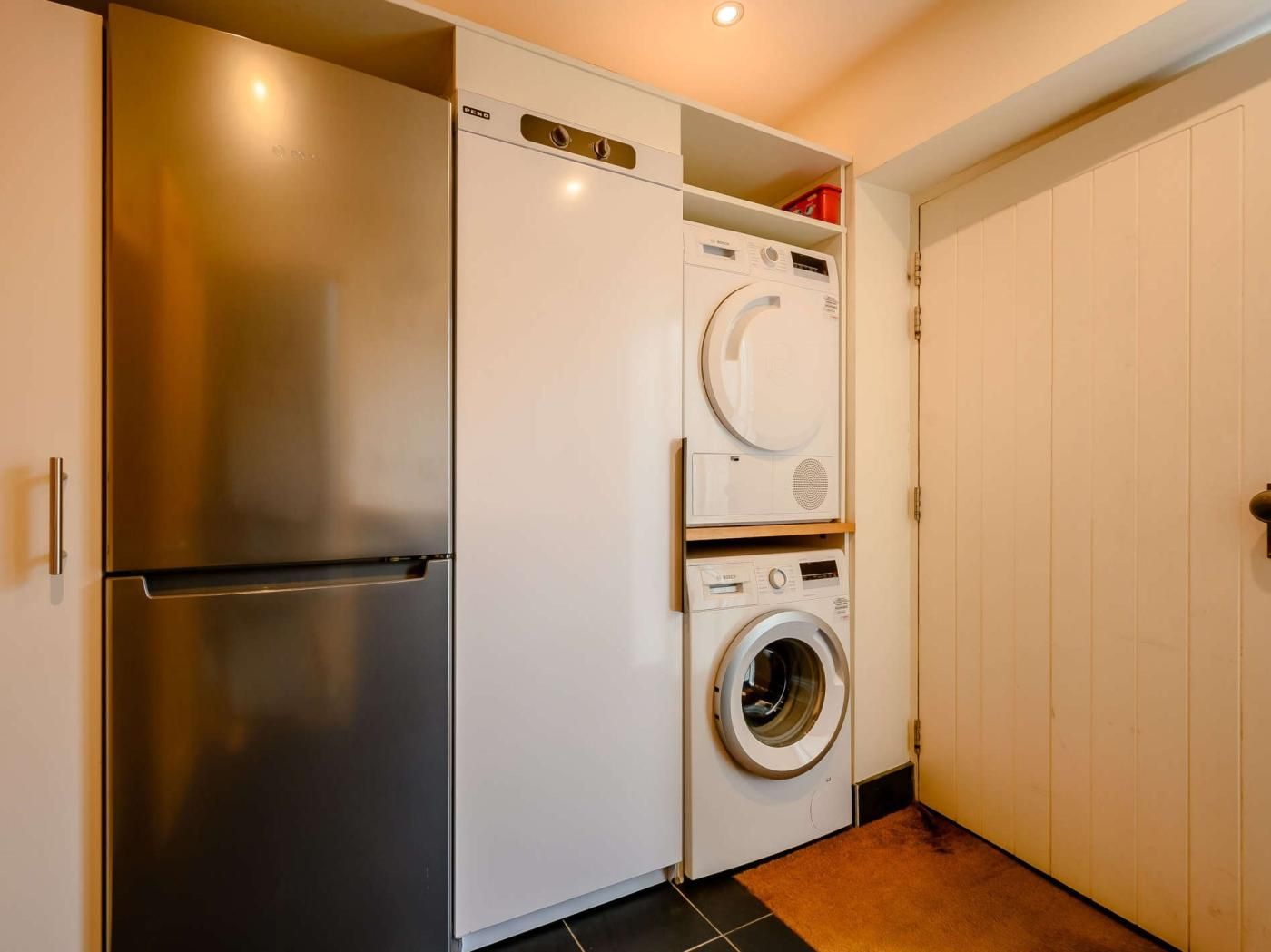 Una cocina compacta con refrigerador de acero inoxidable, lavadora integrada y despensa con estantes.