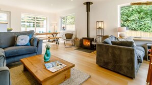 A cozy living room with a fireplace, sofas, a coffee table, and a view of greenery outside. - 4 Bed in Newquay (oc-89241) (Newquay)