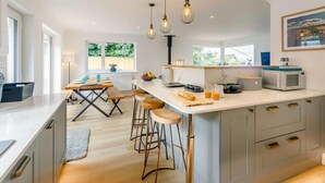 A modern kitchen with a central island, bar stools, and pendant lighting. - 4 Bed in Newquay (oc-89241) (Newquay)