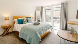 A bedroom with a bed, bedside tables, a round table, and a view through a glass door. - 4 Bed in Newquay (oc-89241) (Newquay)