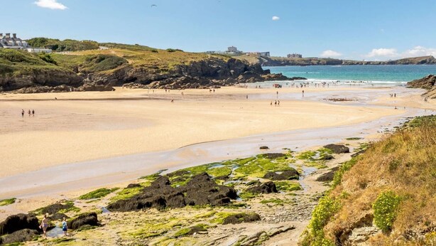 A coastal beach with rocky outcrops, a sandy shore, and buildings in the background. - 4 Bed in Newquay (oc-89241) (Newquay)