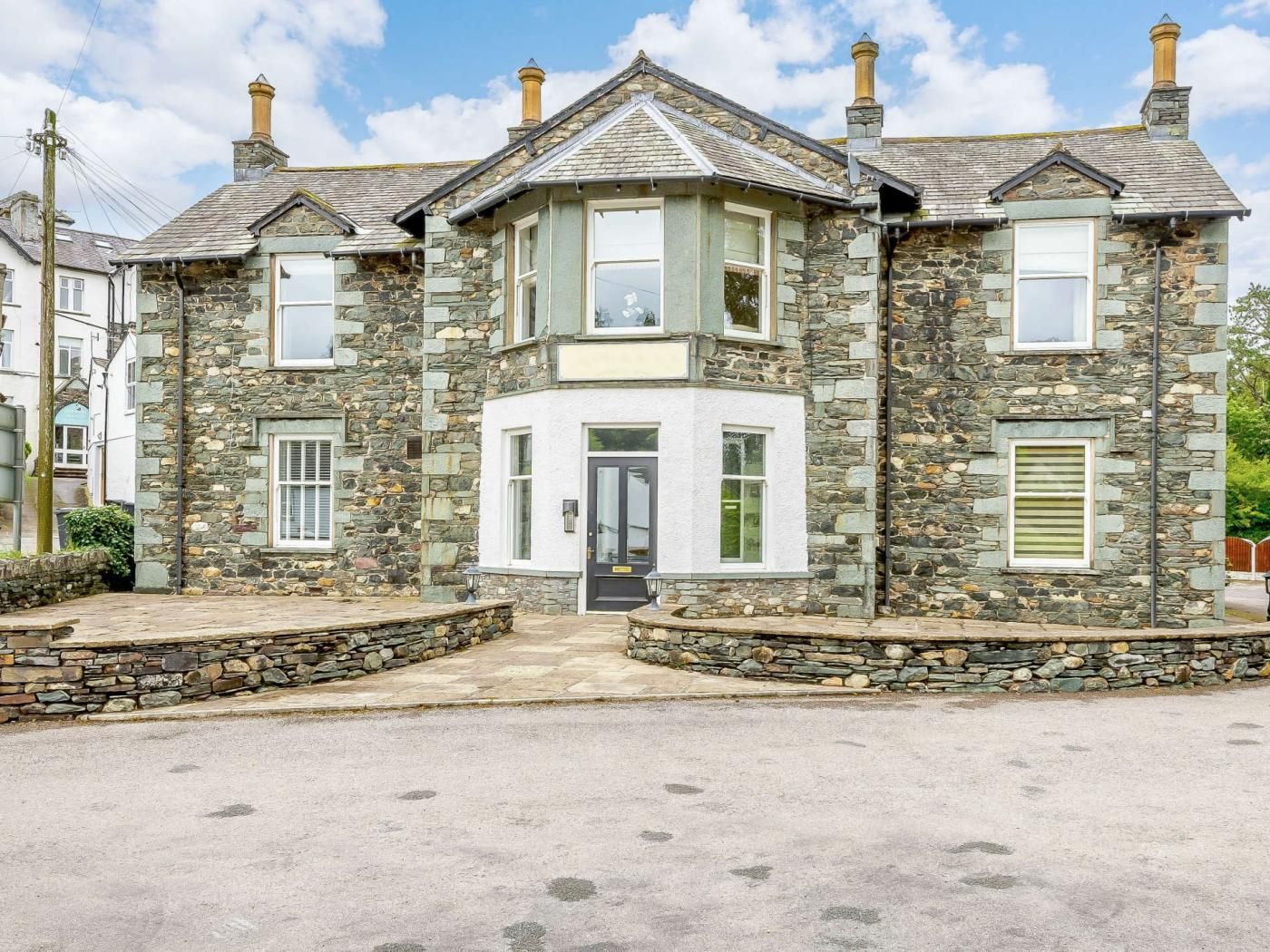 A stone house with a central bay window, a front door, and a small porch area.