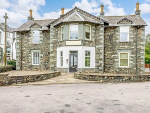 A stone house with a central bay window, a front door, and a small porch area. - 2 Bed in Keswick (oc-89261) (Portinscale)