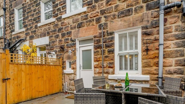 Een stenen huis met een houten poort, een glazen tafel met rieten stoelen, en een fles op tafel.