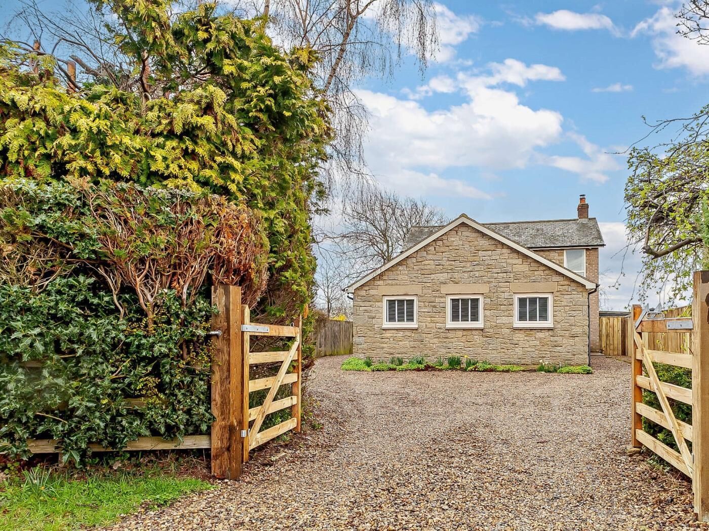 A stone house with a gravel driveway and wooden gates.