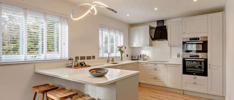 Una cocina moderna con una isla central, taburetes de madera, armarios blancos y electrodomésticos integrados.