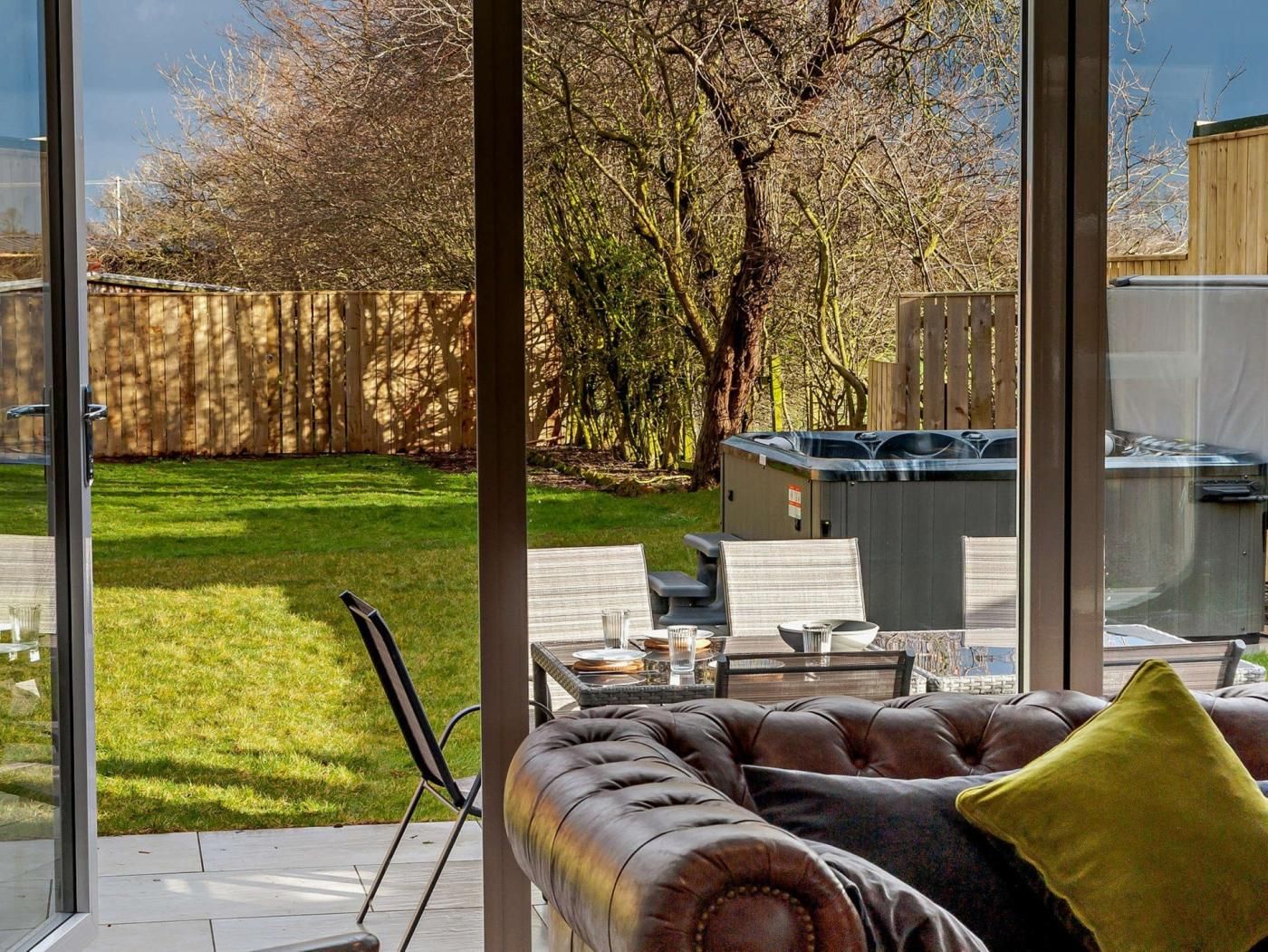 Un soggiorno moderno con un divano in pelle e una parete vetrata che si affaccia su un giardino con una vasca idromassaggio e una recinzione in legno.