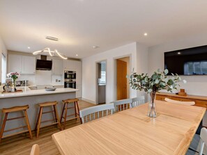 A modern kitchen with white cabinets, a central island, wooden stools, and a dining table. - 4 Bed in Alnwick (oc-89964) (Christon Bank)