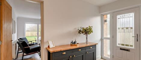 Un couloir avec une armoire en bois foncé, une porte dotée de panneaux en verre dépoli et une vue sur une pièce où l’on aperçoit une chaise et une table.