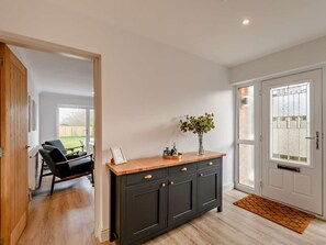 Un pasillo con un armario de madera oscura, una puerta con paneles de vidrio esmerilado y vistas a una habitación con una silla y una mesa.