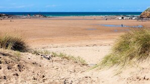 Une vaste plage de sable, avec un phare visible au loin, un ciel bleu dégagé et une mer calme.