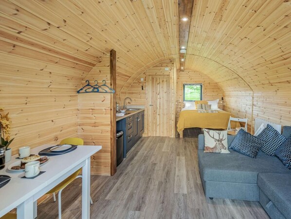 En ombonad inredning med träpanel och en matplats, ett kök och en soffa med mönstrade kuddar.