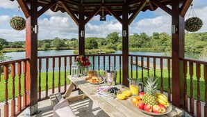 A wooden deck with a table set for breakfast, overlooking a lake.