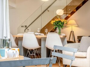 A modern dining area with a table set for two, two white chairs, a vase with yellow flowers, and a lamp. - 2 Bed in Keswick (oc-89257) (Keswick)