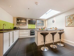 A modern kitchen with a skylight, a central island with bar stools, and a dining area. - 2 Bed in Keswick (oc-89257) (Keswick)