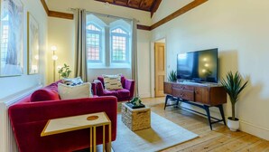 Uma sala de estar com um sofá vermelho, uma televisão em um armário de madeira e uma janela grande com cortinas.
