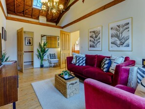 A living room with a red sofa, a woven coffee table, and a wooden floor. There are framed pictures on the wall and a ceiling fan. - 3 Bed in Ventnor (oc-89800) (Ventnor)