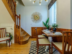 A dining area with a wooden staircase, a sunburst mirror, and a dining table set for four. - 3 Bed in Ventnor (oc-89800) (Ventnor)