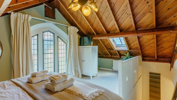 Quarto com teto estilo loft, uma cama com toalhas, janela com cortinas e um armário branco.