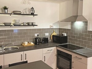 A modern kitchen with a built-in oven, a microwave, a toaster, and a coffee maker on the counter. - 1 Bed in Tenby (oc-89847) (Penally)