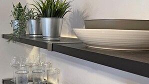 A kitchen shelf with potted plants, a white bowl, and clear drinking glasses. - 1 Bed in Tenby (oc-89847) (Penally)