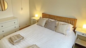 A neatly made bed with pillows and folded towels, a bedside table with a lamp, and a wardrobe with a mirror. - 1 Bed in Tenby (oc-89847) (Penally)