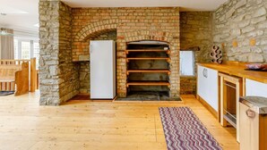 A kitchen with a stone wall, wooden shelves, a refrigerator, and a wooden dining area. - 3 Bed in Coleford (oc-89806) (Coleford)