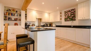A modern kitchen with white cabinetry, a black countertop, and a wooden beam ceiling. - 3 Bed in Cheltenham (oc-89850) (Bourton-on-the-Water)