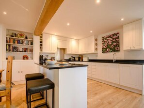 A modern kitchen with white cabinetry, a black countertop, and a wooden beam ceiling. - 3 Bed in Cheltenham (oc-89850) (Bourton-on-the-Water)