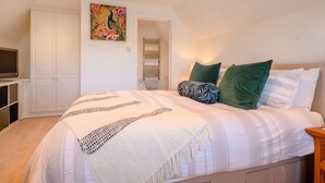 A bedroom with a bed, a TV, a wardrobe, and a painting on the wall. - 3 Bed in Cheltenham (oc-89850) (Bourton-on-the-Water)