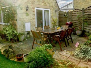 A patio with a wooden table and chairs, surrounded by potted plants and a brick wall. - 3 Bed in Cheltenham (oc-89850) (Bourton-on-the-Water)