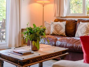 A cozy living room with a leather sofa, a wooden coffee table, and a potted plant. - 3 Bed in Cheltenham (oc-89850) (Bourton-on-the-Water)
