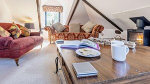 Een knus loft slaapkamer met een schuine plafond, een open haard, een rode bank, een gestreept sofa, en een houten tafel met boeken en een mok.