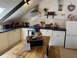 A kitchen with a wooden table, a welcome sign, a toaster, a kettle, and a white refrigerator. - 4 Bed in Bodmin (oc-90215) (Lanhydrock)