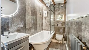Een moderne badkamer met een vrijstaand bad, een toilet en een wastafel met spiegel.