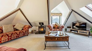 Een loft-achtige woonkamer met een bank, fauteuil, salontafel, televisie en een open haard.