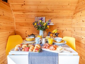 A wooden cabin interior with a dining table set for breakfast, including croissants, fruit, and a variety of beverages.