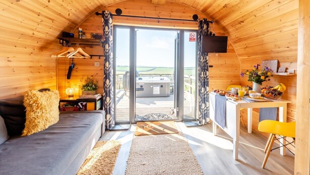Un chalet confortable avec un intérieur en bois, un canapé, une table  à manger où le petit-déjeuner est servi, et un jacuzzi à l’extérieur.