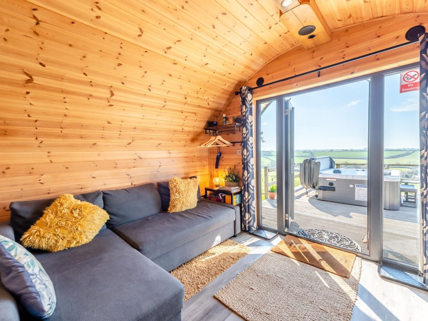 A cozy cabin interior with a sofa, cushions, a lamp, and a view of the outdoors through a sliding glass door.