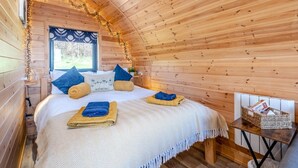 Une chambre confortable, aménagée dans un chalet en bois, avec un lit, des oreillers, une petite table et une fenêtre donnant sur un paysage agréable.