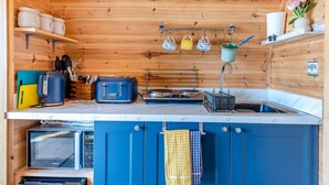Une cuisine compacte aux murs en bois, dotée d’un plan de travail bleu, d’un four à micro-ondes, d’un grille-pain et d’ustensiles suspendus.