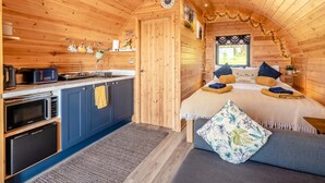 L’intérieur d’un chalet accueillant, avec un plafond en bois, un coin cuisine équipé d’appareils électroménagers, un lit avec des oreillers et une fenêtre.
