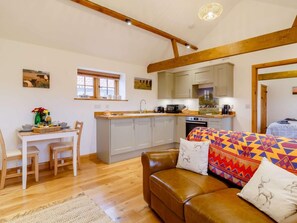 A cozy living room with a brown leather sofa, a dining area with a wooden table and chairs, and a kitchen with light-colored cabinets and a window. - 1 Bed in Beccles (oc-90192) (Burgh Saint Peter)