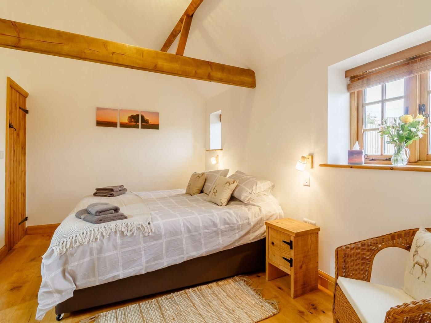 Une chambre à coucher avec un lit, des tables de chevet, une chaise, une fenêtre donnant sur un beau paysage et un tableau accroché au mur.