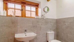 Ein Badezimmer mit einem Standwaschbecken, Toilette und einem Fenster mit Jalousien.