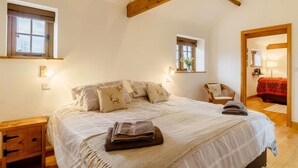Ein Schlafzimmer mit einem großen Bett, zwei Nachttischen, einem Sessel und einem Fenster.