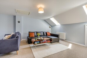 A modern living room with a black leather sofa, a blue armchair, and a coffee table with books and a vase of flowers. - 2 Bed in Cromer (oc-90187) (Cromer)